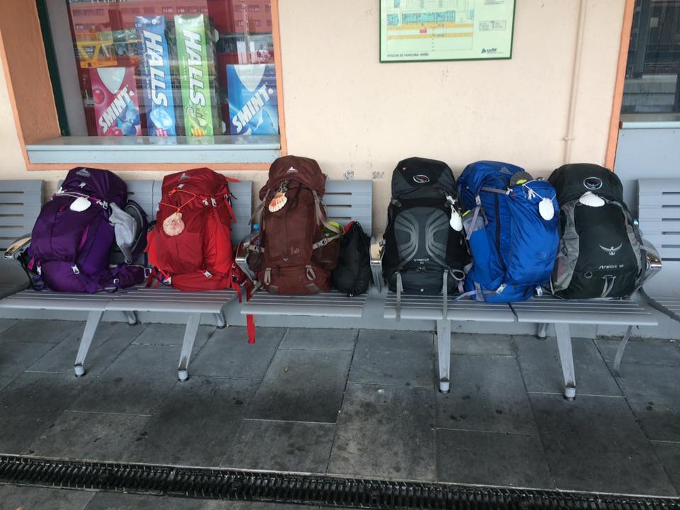 6 backpacking backpacks on a bench at a train station in France. Each backpack has a shell on the front signifying the Camino de Santiago.
